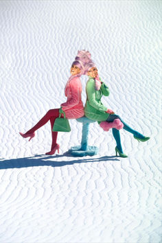 two women sitting on top of each other in the snow with their feet up and one holding her head