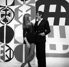 a man and woman standing next to each other in front of a wall with abstract designs