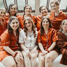 a group of women sitting next to each other on top of a bed in orange robes