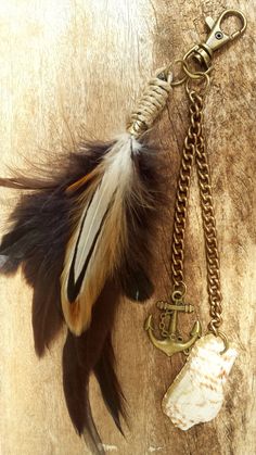 a feather keychain hanging from a chain on a piece of wood with an anchor charm attached to it