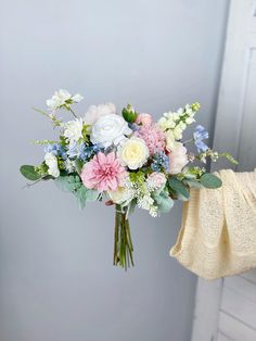 a bouquet of flowers is held up by someone's hand in front of a gray wall