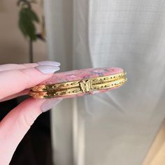 a person holding a pink and gold piece of jewelry