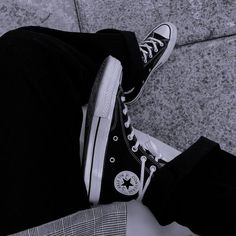 a person wearing black and white converse shoes with their legs crossed on the ground in front of them