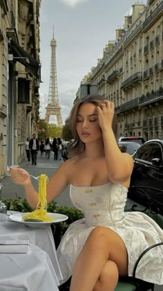 a woman sitting at a table eating spaghetti in front of the eiffel tower