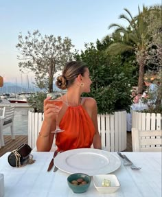 a woman sitting at a table with a glass of wine in her hand and plates on the table