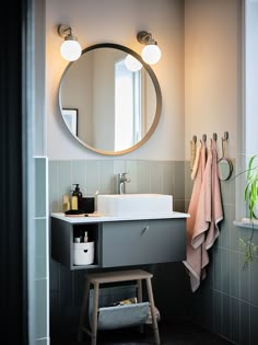 a bathroom sink sitting under a mirror next to a wooden stool and potted plant