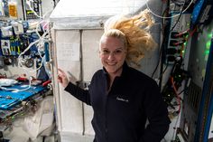 a woman with blonde hair standing in front of a large white object and pointing at the camera