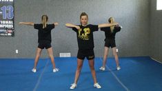 three girls in black shirts and shorts standing on a blue mat with their arms outstretched