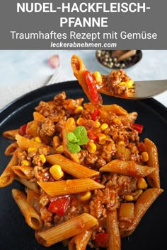 a black plate topped with pasta covered in chili sauce and corn next to a fork