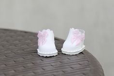 pair of white shoes with pink bows on them sitting on top of a brown chair