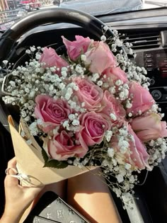 a bouquet of pink roses sitting on top of a steering wheel in front of a car