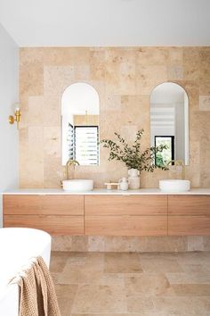 Coastal bathroom with louvre windows, twin basins on a timber vanity with arched mirrors. Travertine floor tiles wrap up the wall to the ceiling on one wall. Travertine Bathroom, Mediterranean Bathroom, Mediterranean Interior, Coastal Bathrooms, Bathroom Renos, House Inspo