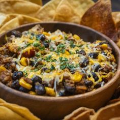 a wooden bowl filled with black beans and corn next to tortilla chips on a table