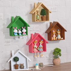 three colorful birdhouses are hanging on the wall next to potted plants and books