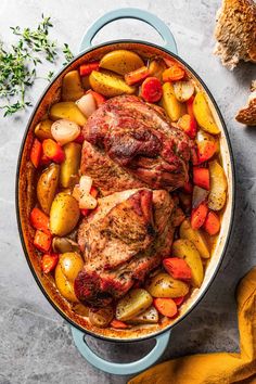 two pork chops with potatoes and carrots in a blue pot next to bread