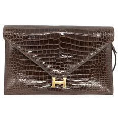 Hermès Brown Crocodile Lydie Crossbody Envelope Shoulder Bag, 1980. This collectors piece is truly an exceptional representation of the Hermès craftsmanship and attention to detail. The structure of the Lydie is bold and elegant, perfect for formal occasions and finished from exotic rich brown crocodile skin. The iconic "H” symbol push lock front closure opens to a supple calfskin leather lined roomy interior with one main compartment complete with zip and slip pocket as well as separate front s H Symbol, Crocodile Skin, 24kt Gold, Box Bag, Brass Hardware, Fashion Handbags, Purses Crossbody, Calf Skin, Dust Bag