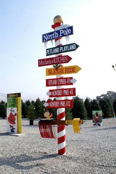 a pole with many different signs on it in the middle of a parking lot next to trees