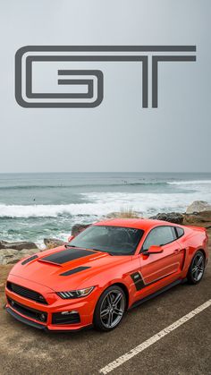 an orange mustang parked in front of the ocean