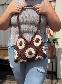 a woman holding onto a brown and white crocheted bag with flowers on it