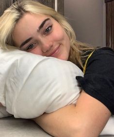 a woman with blonde hair and blue eyes is laying down on a bed while smiling at the camera