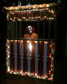 a man wearing a clown mask standing in front of a fence with lights on it