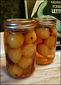 two jars filled with pickles sitting on top of a table next to a book