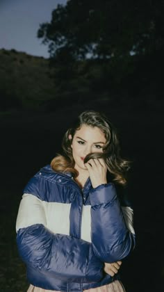 a woman standing in the dark with her hand on her mouth and looking at the camera