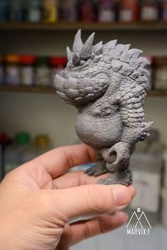 a hand is holding a small toy that looks like a godzilla