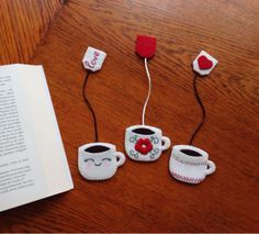 an open book sitting on top of a wooden table next to two coffee mugs