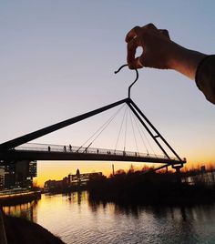 a hand holding a long piece of metal over a body of water with a bridge in the background