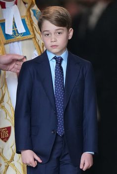 a little boy in a suit and tie standing next to a person wearing a crown