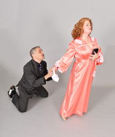 a man kneeling down next to a woman in an orange dress and black suit,