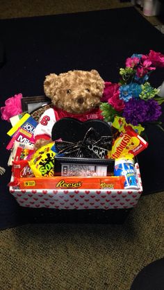 a teddy bear sitting in a candy box filled with candies and other items on the floor