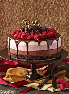 a chocolate cake with raspberries on top is sitting on a table next to red ribbon