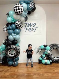 a young boy standing in front of a balloon arch with the letter two fast on it