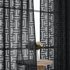 black and white patterned curtains in front of a window with a wooden table next to it