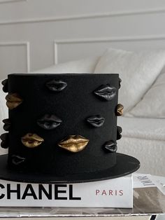 a black cake with gold lips on top sitting on a stack of books next to a white couch