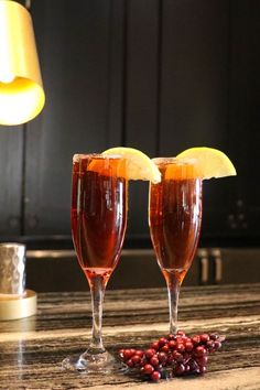 two wine glasses filled with liquid and garnished with orange slices on a table