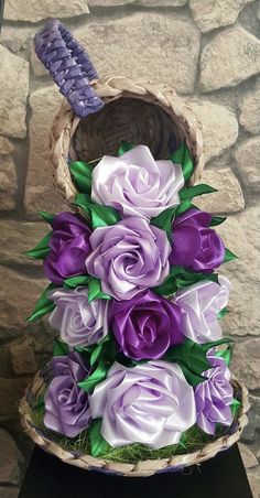 purple and white flowers in a basket on top of a black table next to a stone wall