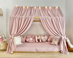 a pink canopy bed with pillows and lights on the top, in a girls'bedroom