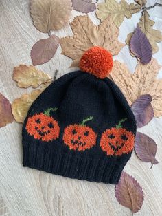 a knitted hat with three pumpkins on it and leaves scattered around the surface