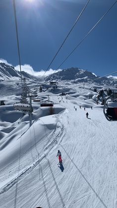 skiers are skiing down a snowy hill under a ski lift with mountains in the background