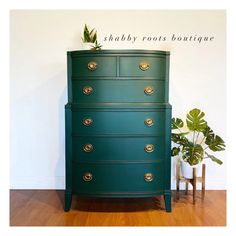 a green chest of drawers sitting on top of a wooden floor next to a potted plant