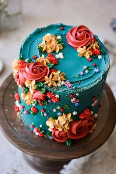 a blue cake with red and yellow flowers on it sitting on a wooden table top