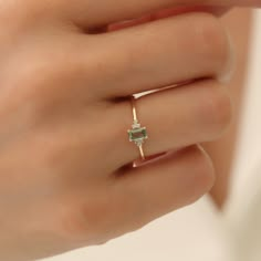 a woman's hand wearing a gold ring with an emerald and diamond set in the middle