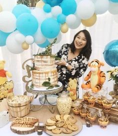 a woman standing in front of a table filled with cookies and desserts, including a winnie the pooh cake