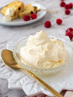 a glass bowl filled with whipped cream and raspberries next to a gold spoon