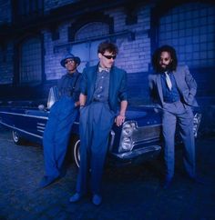 three men in suits standing next to a car