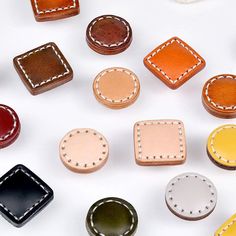 leather buttons with stitching on them are arranged in different colors and sizes, along with white stitching