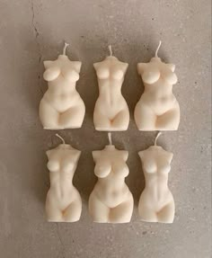 six candles shaped like female nude torsos on a gray surface with one candle in the shape of a woman's breast